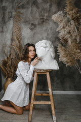 Beautiful curly girl kissing a white plaster head