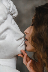 Beautiful curly girl kissing a white plaster head