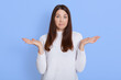 © sementsova321 - Indoor shot of puzzled woman keeps hands spreading aside, looks with doubtful expression, cant make decision, poses over blue background with, girl with puzzled expression looks at camera.