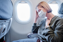 COVID-19 Young Woman With Face Mask Feeling Unwell On Plane. Fear Of Flying Woman In Airplane. Stress, Headache, Motion Sickness And Airsickness On Plane During Pandemic.