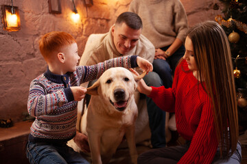 Wall Mural - A happy family of four and a dog celebrate the New Year. Dad, mom, son and daughter love the dog and have fun against the Christmas tree. Labrador and kids.