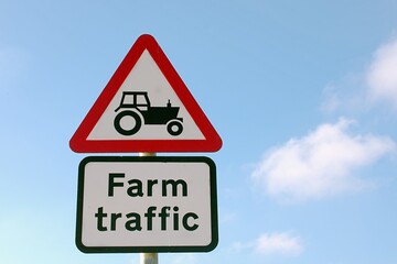 Triangle Road sign with tractor and text Farm traffic, blue cloudy sky