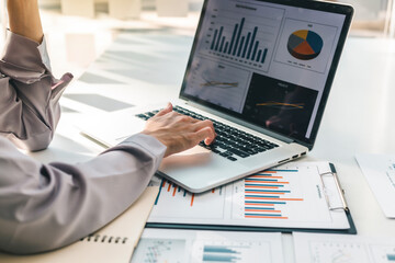 Business women sitting on a laptop and checking business graph documents, working in financial transactions, accounting