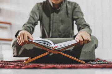 Wall Mural - Crop shot of Muslim Boy reading the holy book Al-Quran on the prayer mat with selective focus photo