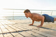 © splitov27 - Muscular handsome fitness man with naked torso doing push-ups on the beach at sunrise