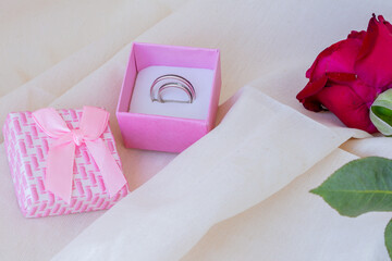 Red rose with water drops and a gift of wedding rings in a box. Linen natural color fabric background. Concept Valentine, gift, romance.