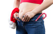 Young woman tries to button tight jeans with Christmas candy cane and Santa hat in pockets. Concept of unhealthy lifestyle and overeating during Christmas. Close shot.