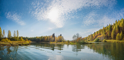 Wall Mural - autumn forest trees are reflected in the river water of the panoramic landscape. blue sky with cloud