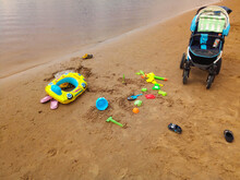 The Concept Of A Beach Holiday For Children. Baby Stroller And Bright Plastic Children's Toys In The Sand. Space For Text
