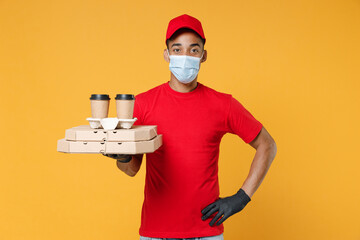 Wall Mural - Delivery employee african man in red cap blank print t-shirt face mask gloves work courier service on quarantine coronavirus covid-19 virus hold cardboard pizza flatbox isolated on yellow background.