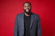 © ViDi Studio - Smiling attractive confident successful young african american business man 20s wearing classic jacket suit standing and looking camera isolated on bright red color wall background studio portrait.