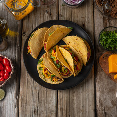 Wall Mural - Plate with tasty mexican tacos on rustic wooden table with ingredients for cooking background. Concept of traditional meal. View from above. Flat lay. Cookbook illustration.