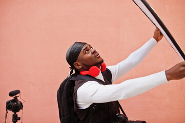 Wall Mural - Young professional african american videographer holding professional camera with pro equipment. Afro cameraman wearing black duraq making a videos.