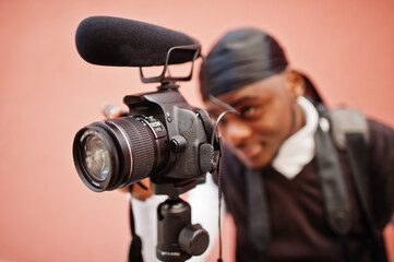 Wall Mural - Young professional african american videographer holding professional camera with pro equipment. Afro cameraman wearing black duraq making a videos.