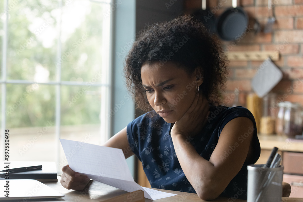Frustrated young african american woman reading paper letter with bad news, stressed of getting bank debt or loan rejection notification, feeling confused of termination notice, sitting at table. - obrazy, fototapety, plakaty 