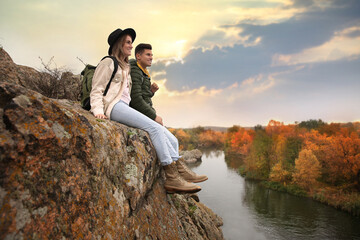 Sticker - Couple of hikers with travel backpacks sitting on steep cliff near mountain river