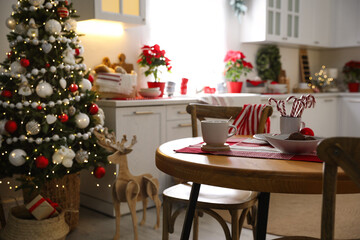 Canvas Print - Cup of drink and candy canes on wooden table near Christmas tree in kitchen interior