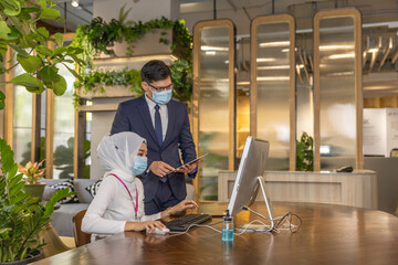 Business in new normal. Young Muslim lady is getting support from her supervisor how to use technology for online business in an environmental friendly office