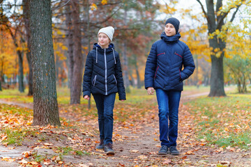 teen girl and boy walking through the park and enjoys autumn, beautiful nature with yellow leaves