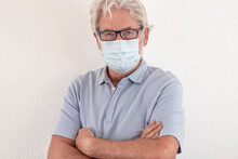Coronavirus. Portrait Of Serious Senior Man Wearing Protective Face Mask Due To Coronavirus Looking At Camera With Crossed Arms