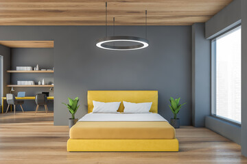 Grey wooden bedroom with yellow bed near window and workplace on background