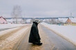 Strange little girl in worn oversized clothes standing at snowy road win winter day in russian village.