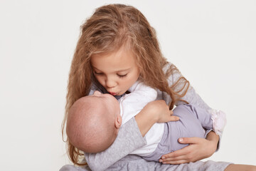 Wall Mural - Happy two sisters children posing together isolated over white background, blond female kid kiss her sibling, wearing casual clothing, family love. Childhood.