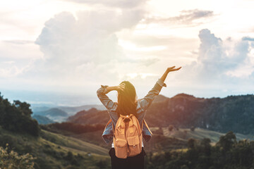 Happy young woman traveler relaxing and looking at the beautiful sunset on the top of mountain