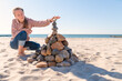 ein junges Mädchen baut am Ostseestrand eine Steinpyramiede im Sand bei Sonnenlicht