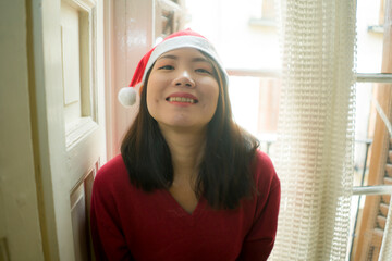 lifestyle home portrait of young beautiful and happy Asian Korean woman in Santa Claus hat and red jersey enjoying Christmas time smiling cheerful