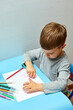 © Мария Чичина - Cute little boy with blond hair draws colored pencils at home. Draws at the blue table.