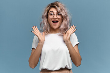 Wall Mural - Overjoyed cute young woman with nose ring gesturing excitedly, opening mouth widely, happy to get amazing unexpected present. Amazed pretty girl in glasses expressing excitement with sale prices