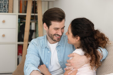 Wall Mural - Close up happy young couple hugging, looking in eyes with love, smiling man and woman cuddling, sitting on cozy couch at home, overjoyed family enjoying tender moment, romantic date, having fun