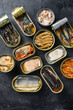 A group of aluminium cans canned with different types of fish and seafood, top view over black textured background