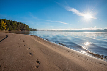 Wall Mural - bare footprints on the sand by the river, sunny morning and fog over the water, sun rays.