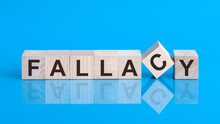 The Text FALLACY Is Written On The Cubes In Black Letters, The Cubes Are Located On A Blue Glass Surface