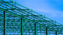 Green Steel Roof Structure Of Warehouse Building In Construction Area Against Blue Sky Background