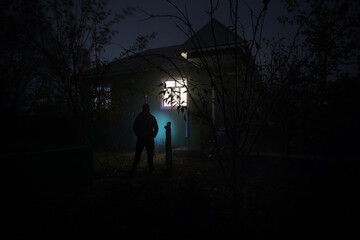 Old house with a Ghost in the forest at night. Horror silhouette at the window. Horror Halloween concept Alone man silhouette standing near window of dollhouse at night. Selective focus