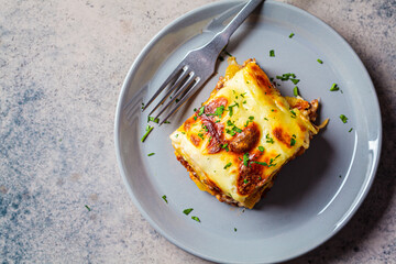 Canvas Print - Portion of  Greek moussaka - potato and meat casserole with cheese on gray plate, dark background, top view. Greek food concept.