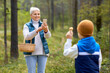 © Syda Productions - picking season, leisure and people concept - happy smiling grandmother with smartphone photographing grandson with mushrooms in basket in forest