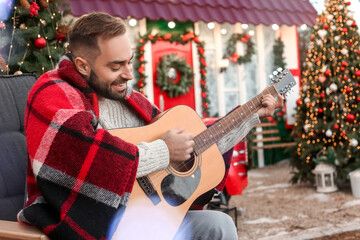 Wall Mural - Young man playing guitar outdoors on Christmas eve