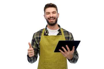 gardening, farming and technology concept - happy smiling male gardener or farmer in apron and rubber boots with tablet pc computer showing thumbs up over white background