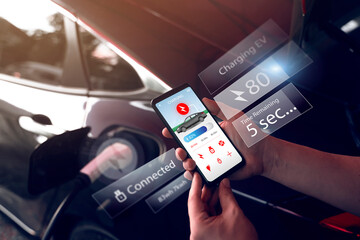 Using mobile smartphone device refueling electric vehicle EV car mock UI application display screen, hand holding cellphone at electric car charging station connected power cable alternative energy