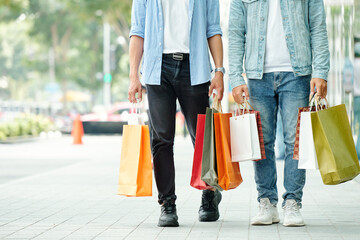 Sticker - Cropped image of young men walking down the street with many shopping bags in hands