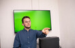 © FarukPhotography - young caucasian businessman wearing glasses points a finger at someone in front of a smart board with a green screen