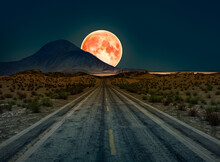 A Desert Road At Night Leading Off Into Infinity With A Huge Full Moon On The Horizon.