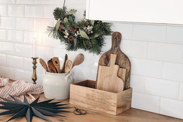 Closeup of kitchen interior. Christmas decoration. Advent floral hoop wreath. Black paper star. White brick wall, metro tiles, wooden countertops with kitchen utensils. Vintage scandinavian design.