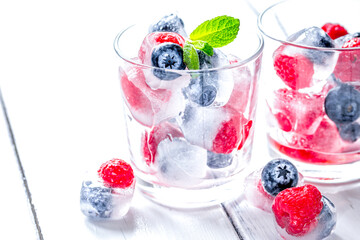 glass with frozen berries in cubes on wooden desk background