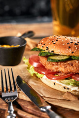 The concept of American fast food. A juicy American burger with two beef patties and a dark beer on a glass table and an orange background. Copy space