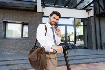 businessman in suit standing near e-scooter with leather bag